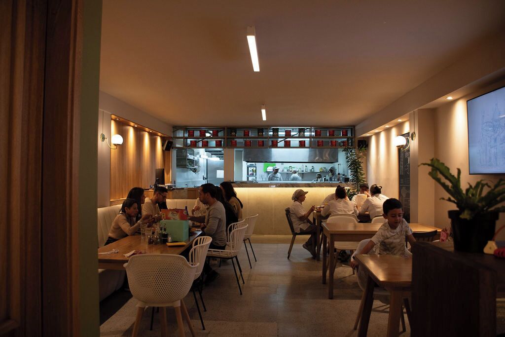 Un restaurant doté d’un long comptoir, de plusieurs tables et de chaises. On aperçoit à l’arrière un espace cuisine avec un comptoir et divers articles exposés.