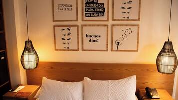 A hotel room with a wooden headboard, a bed with white pillows, two bedside tables with lamps, and motivational wall art.