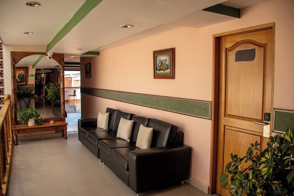 Un área de recepción con un sofá de cuero negro, un banco de madera y una puerta de madera con una placa.