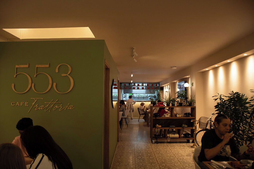 Kahvilan sisustus, jossa on vihreä seinä, jossa näkyy numero 553 ja nimi ”Cafe Trattoria”.