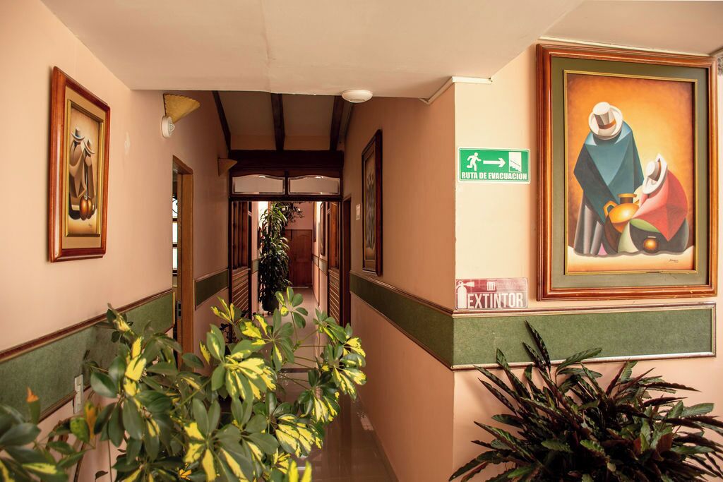 Un pasillo con obras de arte enmarcadas, un letrero de salida verde y un cartel que indica una salida.