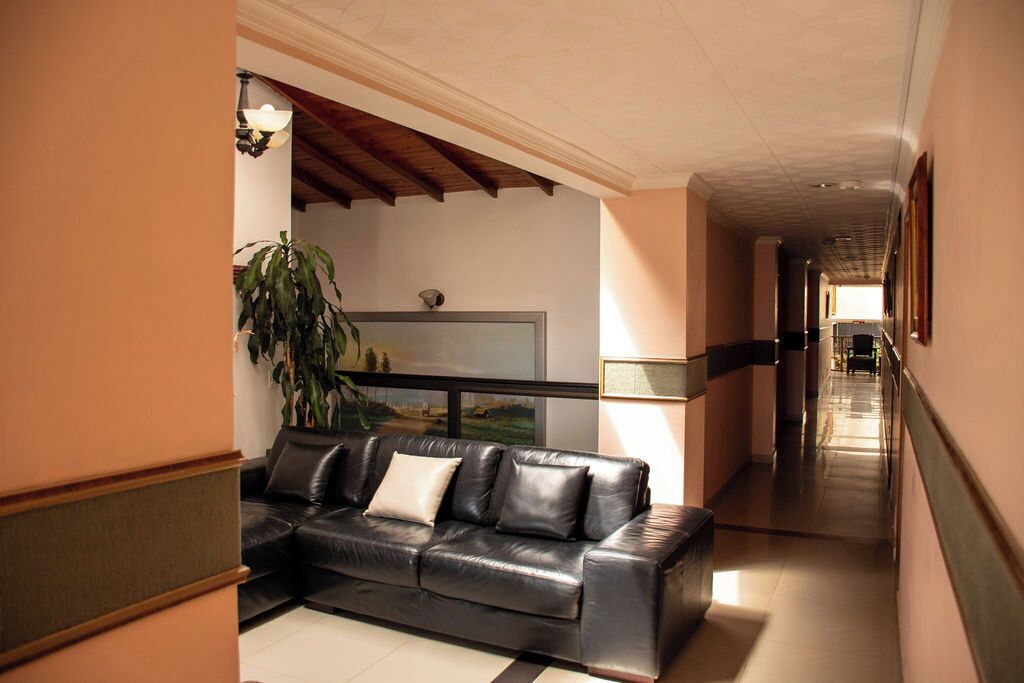 A modern lobby with a black leather sofa, a large potted plant, and a framed artwork on the wall.