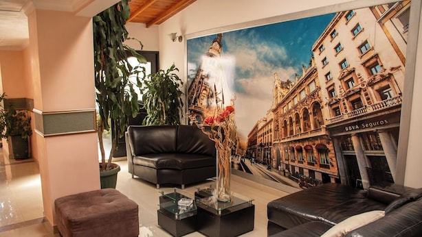 Una sala de estar moderna con un sofá de cuero negro, una mesa de centro de vidrio y un mural grande con un paisaje urbano en la pared.