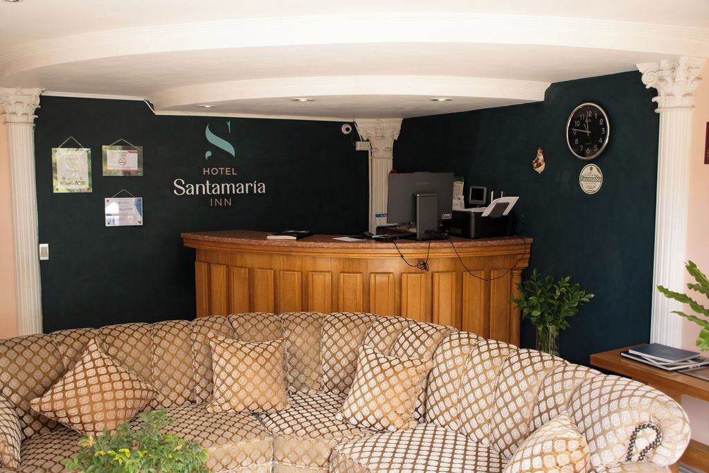 A reception area with a check-in counter, a sofa with patterned cushions, and a clock on the wall.