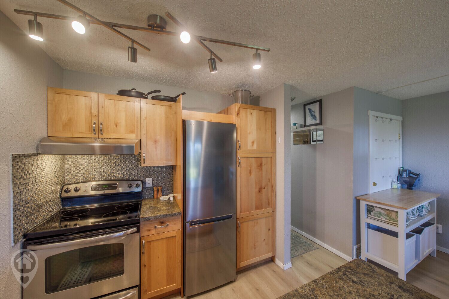 A compact kitchen with wooden cabinets, a stainless steel refrigerator, a stove, and a microwave.