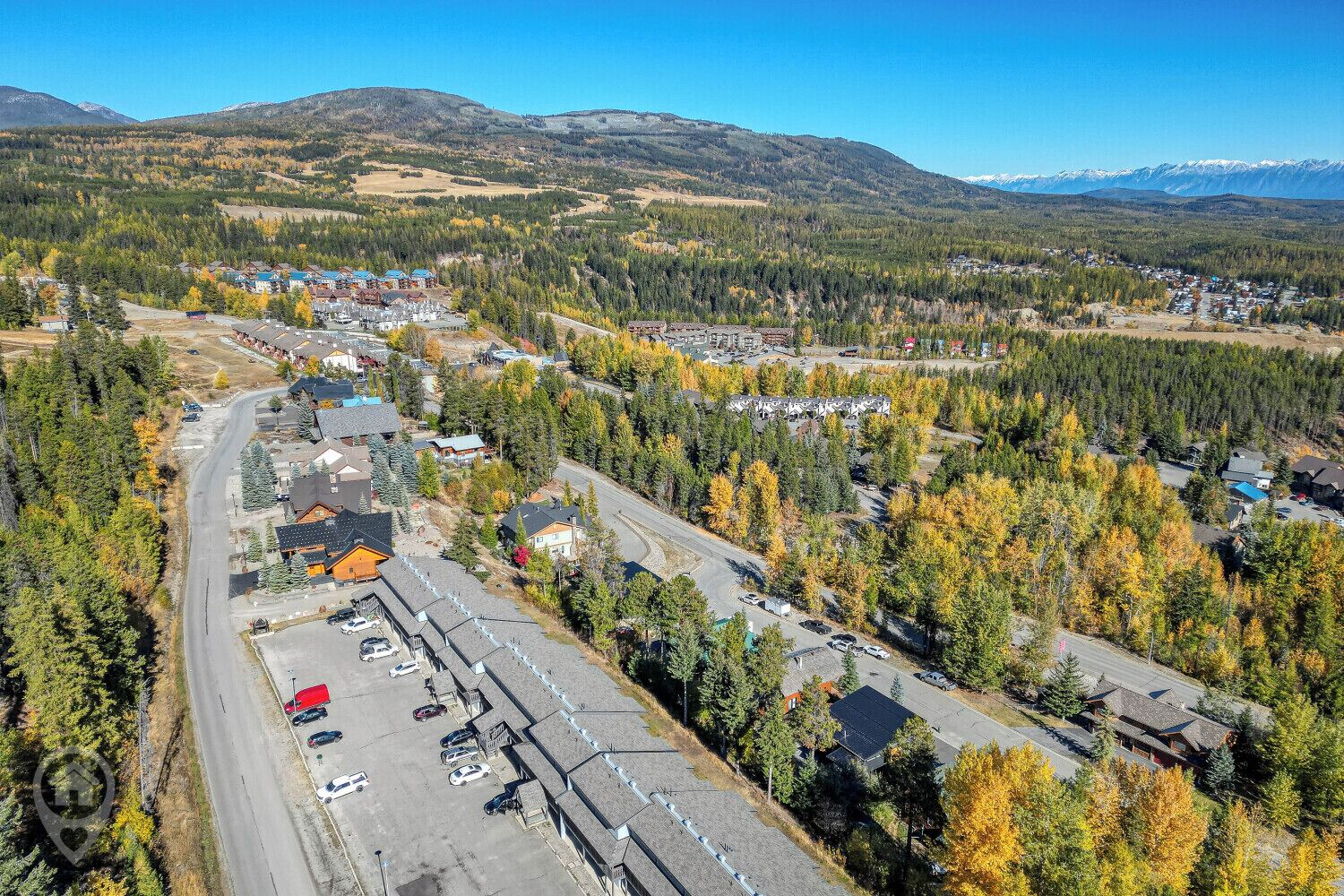 Luchtbeeld van een stad met een grote parkeerplaats, omgeven door dichte bossen en bergen op de achtergrond.