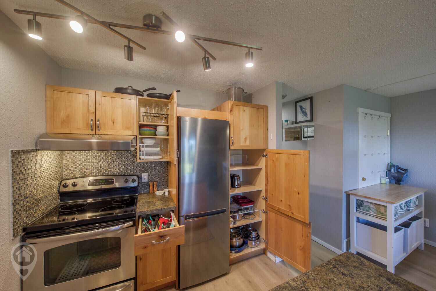 A compact kitchen with wooden cabinets, a stainless steel refrigerator, a built-in oven, and a microwave.