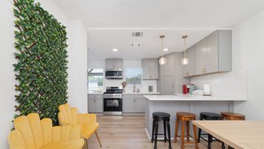 A modern kitchen with grey cabinets, a wooden dining table, and a yellow chair.