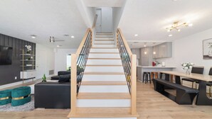 A modern staircase with wooden steps and black railings, leading to a kitchen area with a dining table and bar stools.