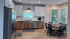 Una cucina moderna con mobili bianchi, frigorifero in acciaio inossidabile, piano di lavoro in legno, lavastoviglie integrata e zona pranzo con tavolo e sedie in legno.