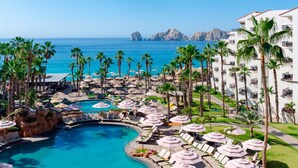 A resort with a pool, palm trees, and a view of the ocean. - 1-Bedroom Medano beach 5* resort ***HURRY***Only available March 14 to 21, 2026 (Cabo San Lucas)