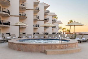 Zona de piscina en la azotea con sillones de descanso y sombrillas, rodeada por un edificio de varios pisos con balcones.