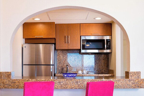 Eine kleine Küche mit einem Edelstahl-Kühlschrank, einer Mikrowelle und Granit-Arbeitsplatten.