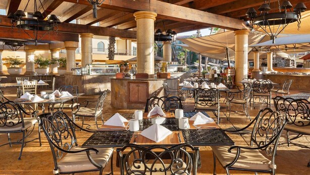 An outdoor dining area with tables and chairs, a central bar, and a view of the surrounding buildings. - 1-Bedroom Medano beach 5* resort ***HURRY***Only available March 14 to 21, 2026 (Cabo San Lucas)