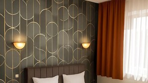 A hotel room with a large bed, two bedside tables, a telephone, and a window with curtains.