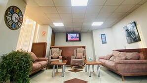A spacious room with a tiled floor, two sofas, a coffee table, a television, and a clock on the wall.
