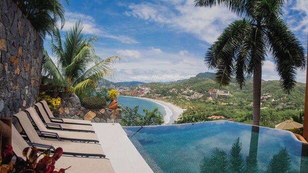 A infinity pool with a view of a beach and mountains. - Zihua Vista Bay Principal: Stunning La Ropa Views, Infinity Pool & Gourmet Kitch (Zihuatanejo)