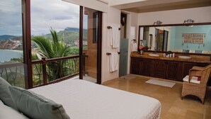 A bedroom with a large bed, a bathroom with a sink and mirror, and a balcony with a view of the landscape. - Zihua Vista Bay Principal: Stunning La Ropa Views, Infinity Pool & Gourmet Kitch (Zihuatanejo)