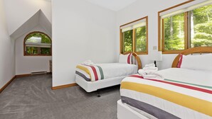 A bedroom with two beds, a skylight, and large windows with a view of trees.