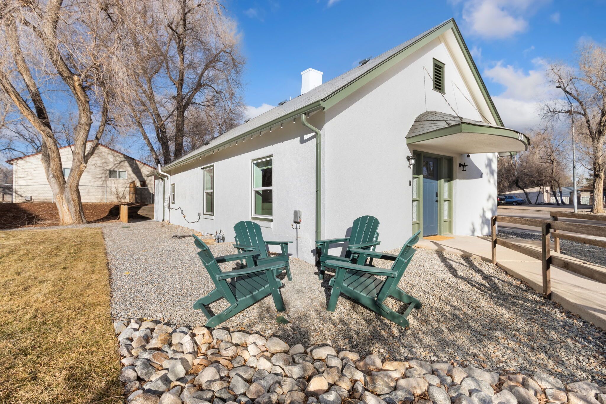 A white building with a green roof, two green Adirondack chairs, and a gravel pathway.