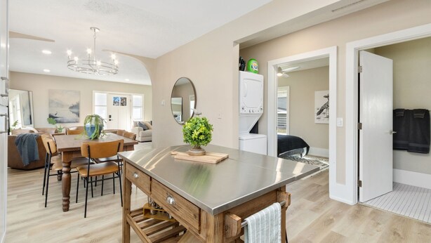 Een moderne keuken met een centraal eiland, houten stoelen, een eettafel en een kroonluchter.