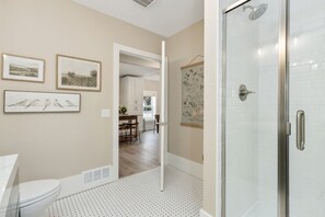 Een badkamer met toilet, een douche met glazen deur, en een gang die leidt naar een eetgedeelte.