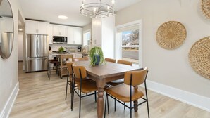 Een moderne keuken met roestvrijstalen apparatuur, een houten eettafel met stoelen en decoratieve wandkunst van geweven materiaal.