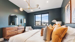 Une chambre avec un grand lit, une commode en bois, une chaise, une fenêtre donnant sur un beau paysage et un luminaire au plafond.