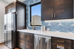 Une cuisine moderne avec des meubles en bois foncé, des appareils électroménagers en acier inoxydable et un revêtement mural à motifs géométriques.