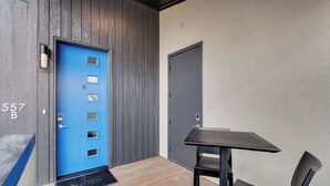 Une pièce moderne avec une porte bleue, un plancher en bois, une table noire avec une chaise et une porte grise.