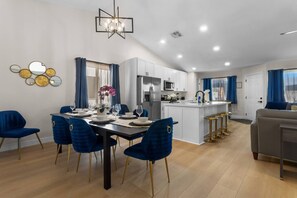 A modern kitchen with white cabinets, a central island, and a dining area with blue chairs. - Vegas Vacation 5BD-Pool, Spa, Games, and More! (North Las Vegas)
