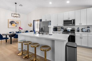 A modern kitchen with white cabinets, a central island with stools, a microwave, stove, and a trash bin. - Vegas Vacation 5BD-Pool, Spa, Games, and More! (North Las Vegas)