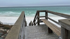 En træbro der fører til en strand med udsigt over havet.