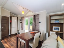 Uma sala de jantar com mesa e cadeiras de madeira, um sofá, uma estante com livros e vista para o verde lá fora.