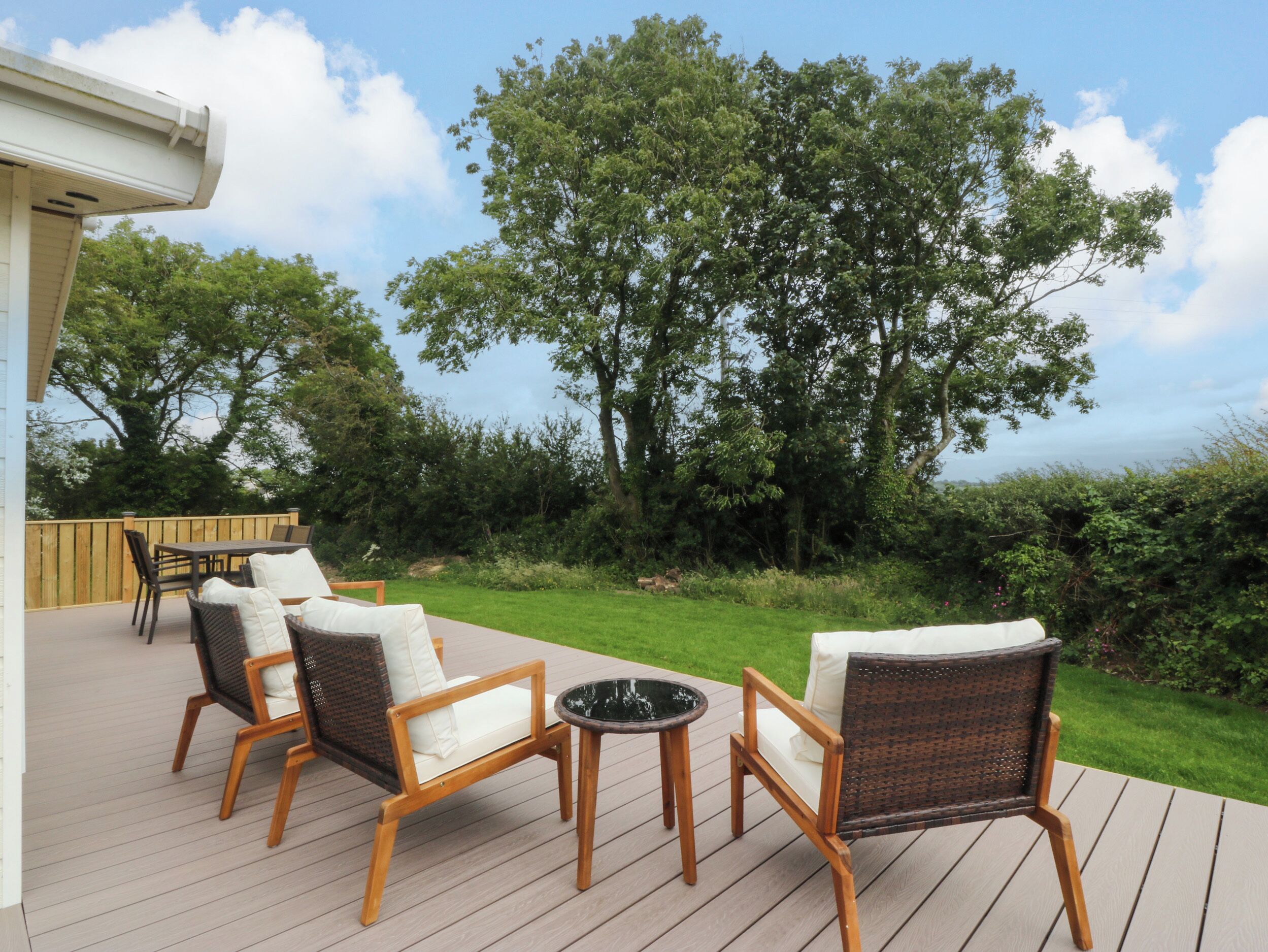 A deck with wicker furniture, a small table, and a view of a grassy area with trees.