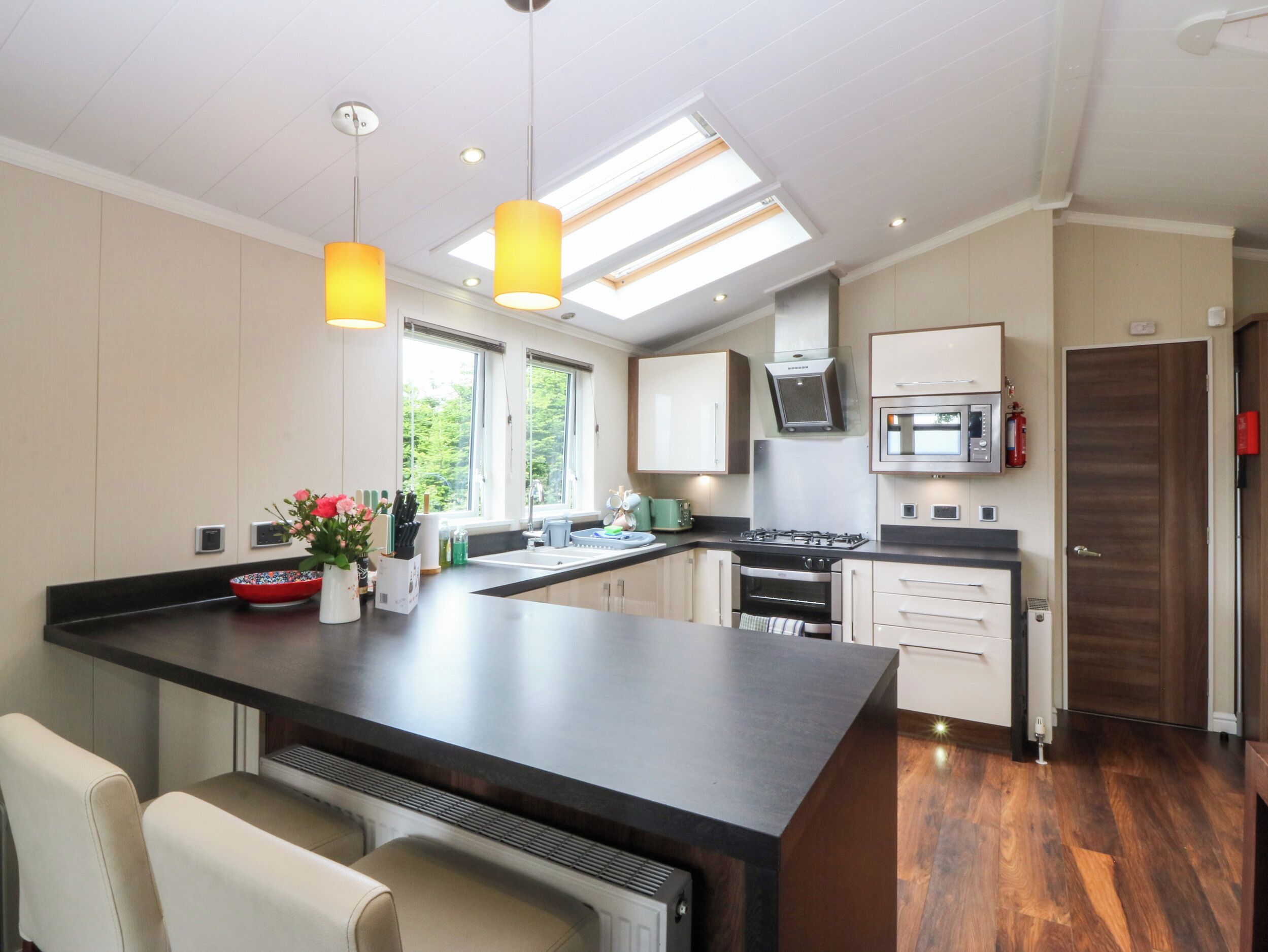 A modern kitchen with a central island, pendant lights, a stove, oven, microwave, and a view of greenery outside.