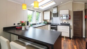 A modern kitchen with a central island, pendant lights, a stove, oven, microwave, and a view of greenery outside. - Plas Marchog Lodge (Pentraeth)
