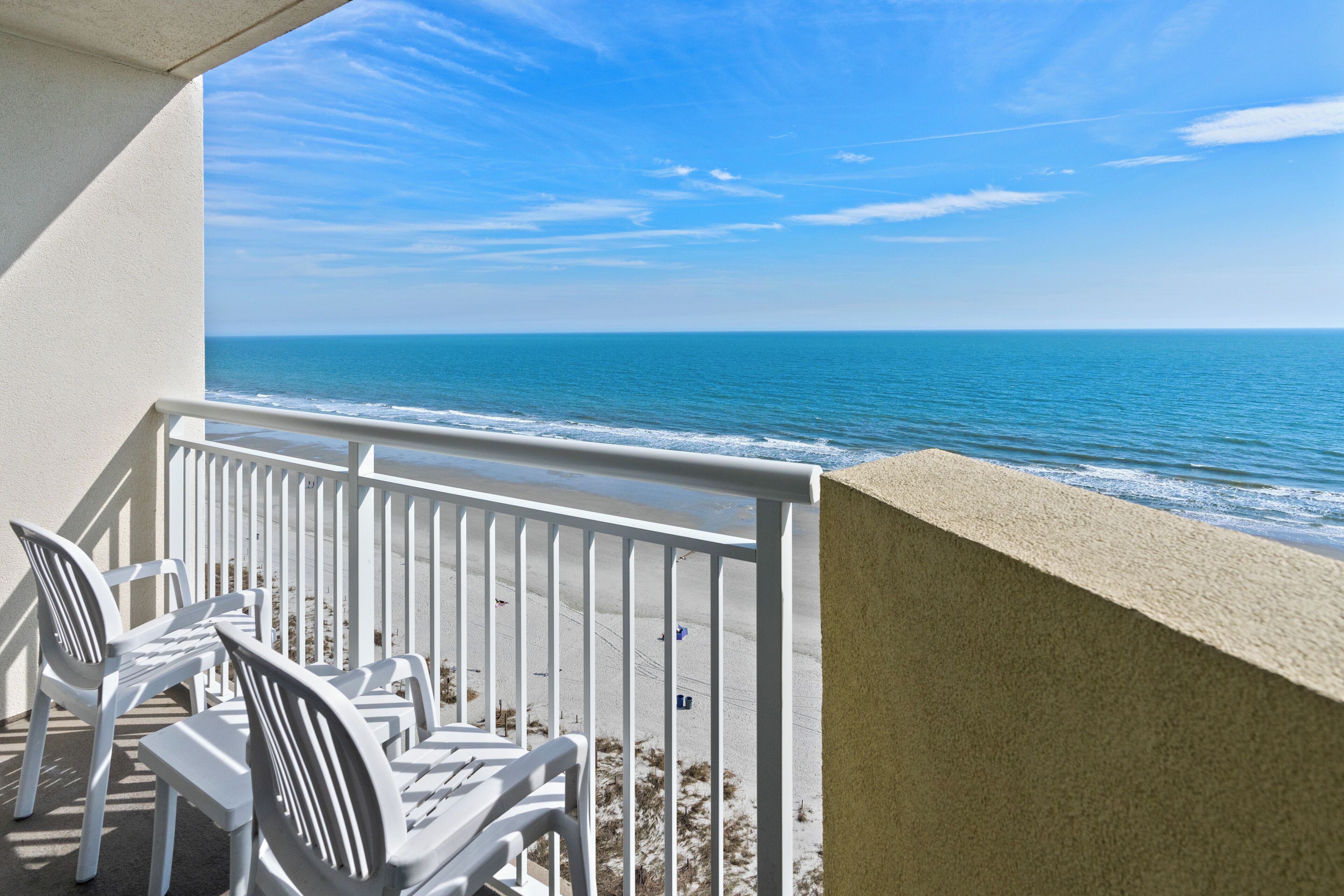 A balcony with white chairs overlooking a beach.