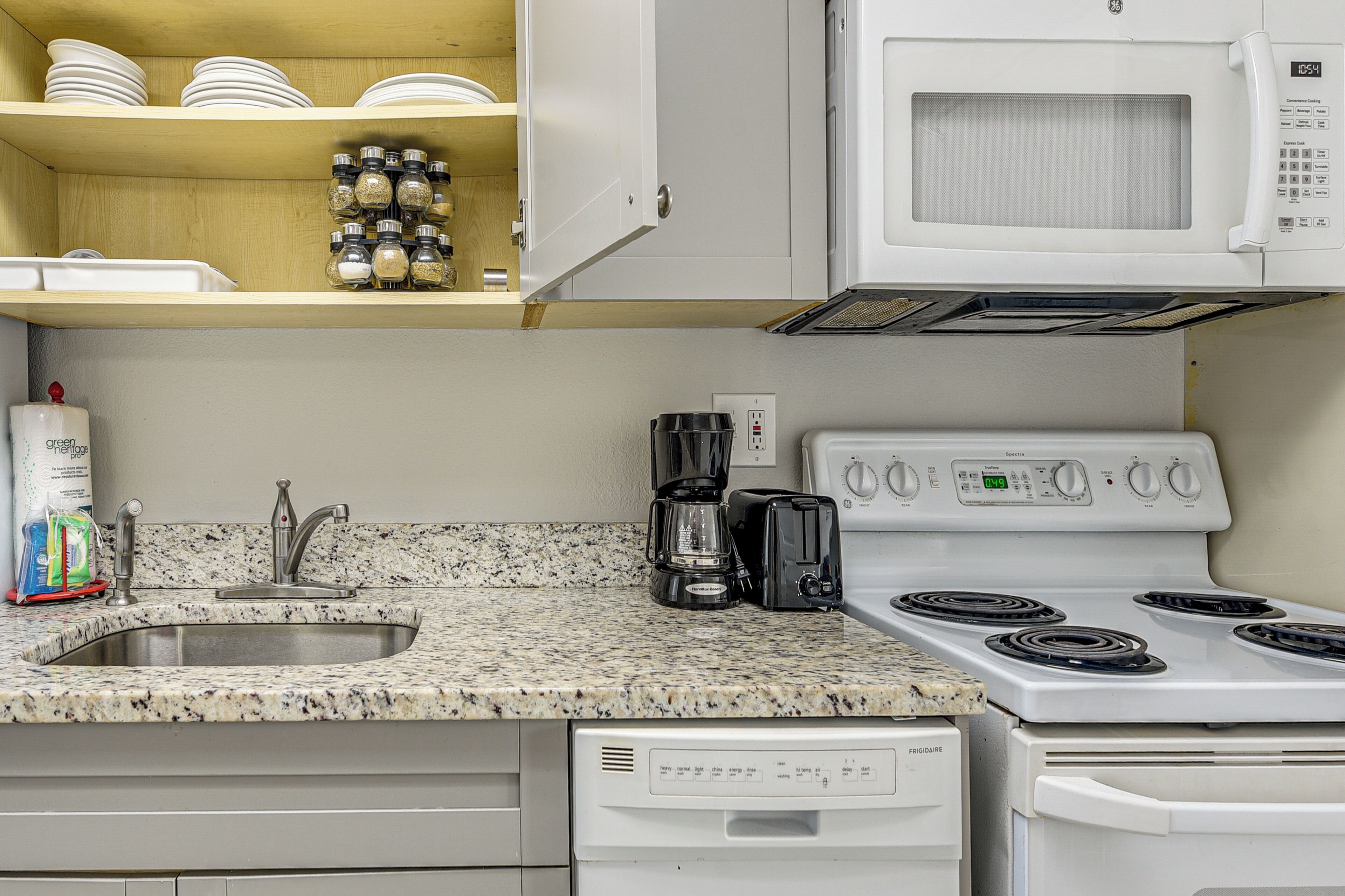 A kitchen with a granite countertop, white cabinets, a microwave, a stove, a coffee maker, and a dishwasher.