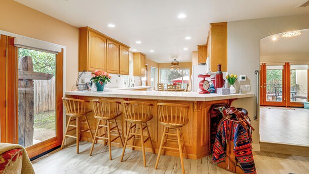 A kitchen with wooden cabinets, a bar area with stools, and a large window. - Hot Tub & Huge Patio: Home 5 Mi to Old Town Auburn (Auburn)