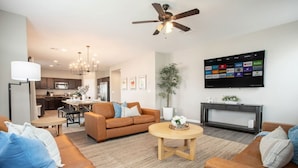A modern living room with a brown sofa, a coffee table, and a TV mounted on the wall displaying streaming services. - Spacious 5BD with Pool Table (North Las Vegas)