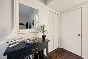 A hallway with a black console table, a potted plant, a decorative bowl, a hanging sailboat, and a closed door. - Marina View Retreat at Shelter Cove Walk to Dining (Hilton Head Island)