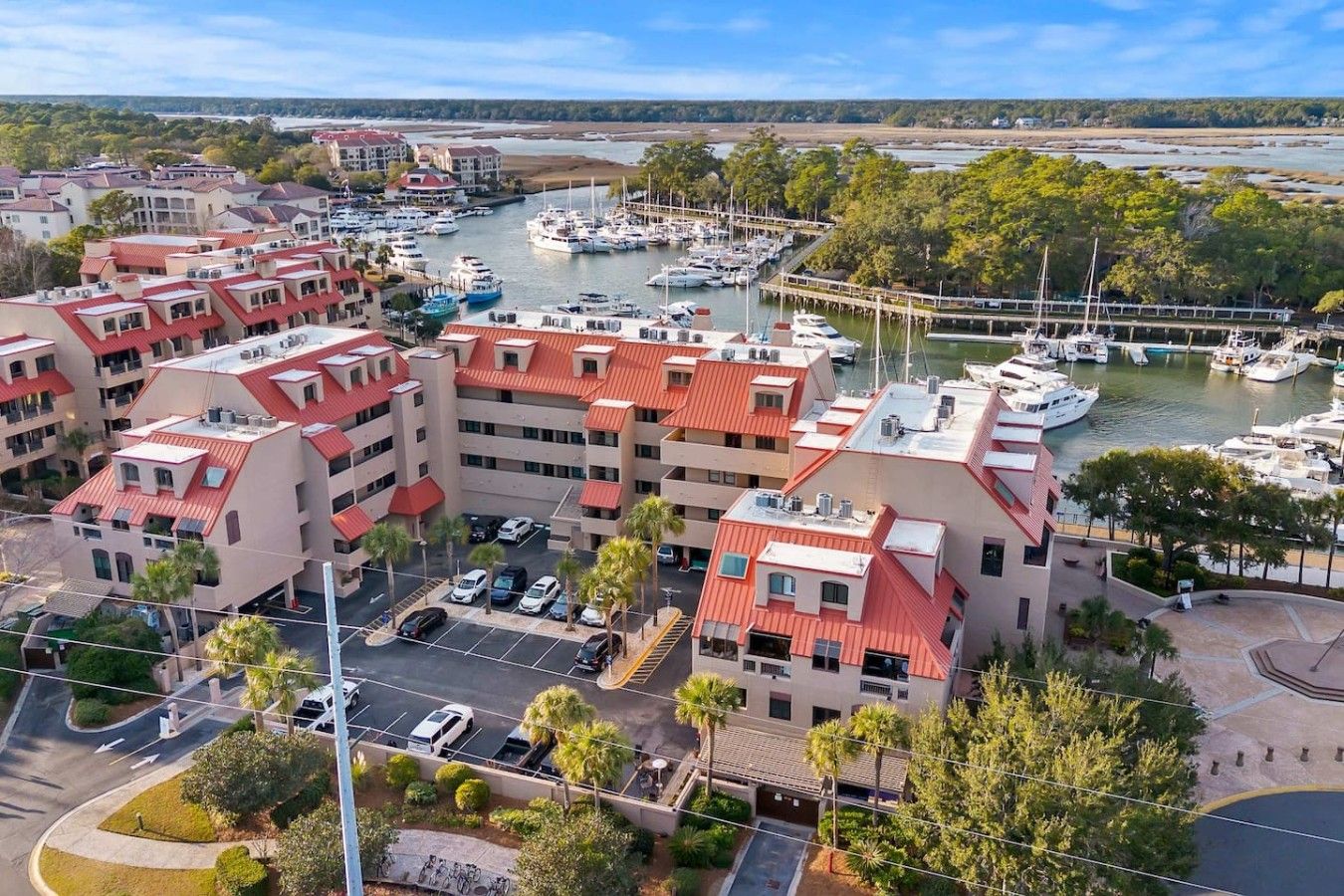 A marina with boats, a parking lot, and a building with red roofs.