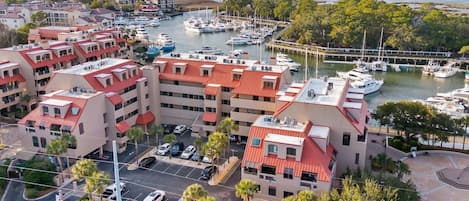 A marina with boats, a parking lot, and a building with red roofs.