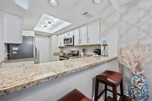 A modern kitchen with white cabinets, granite countertops, a microwave, and a coffee maker. - Marina View Retreat at Shelter Cove Walk to Dining (Hilton Head Island)