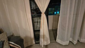 Balcó amb vistes a la ciutat de nit, cortines lligades al centre i una petita zona de seients amb coixí i cadira.