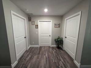 A hallway with two white doors, a potted plant, and framed pictures on the walls. - The Gathering Place at Ft. Wood (Waynesville)