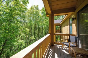 A wooden deck with a chair and table, overlooking a forest.