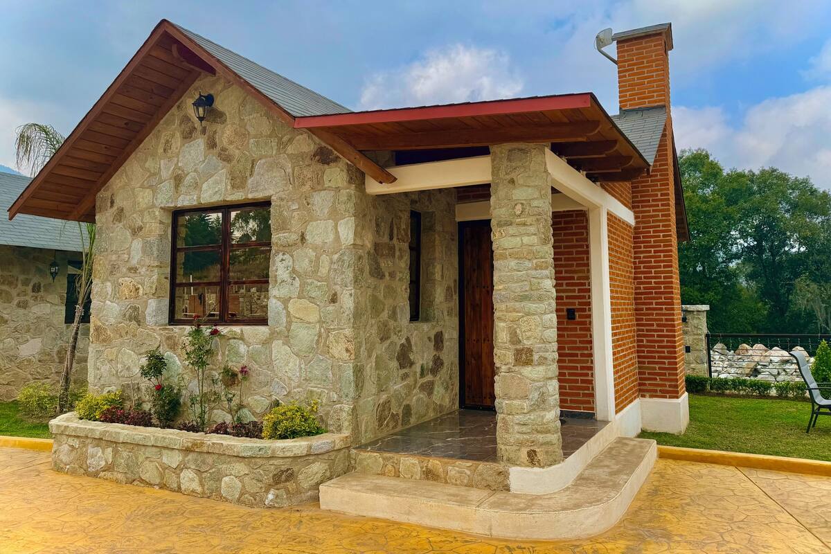 A stone house with a red roof, a wooden porch, and a brick chimney.