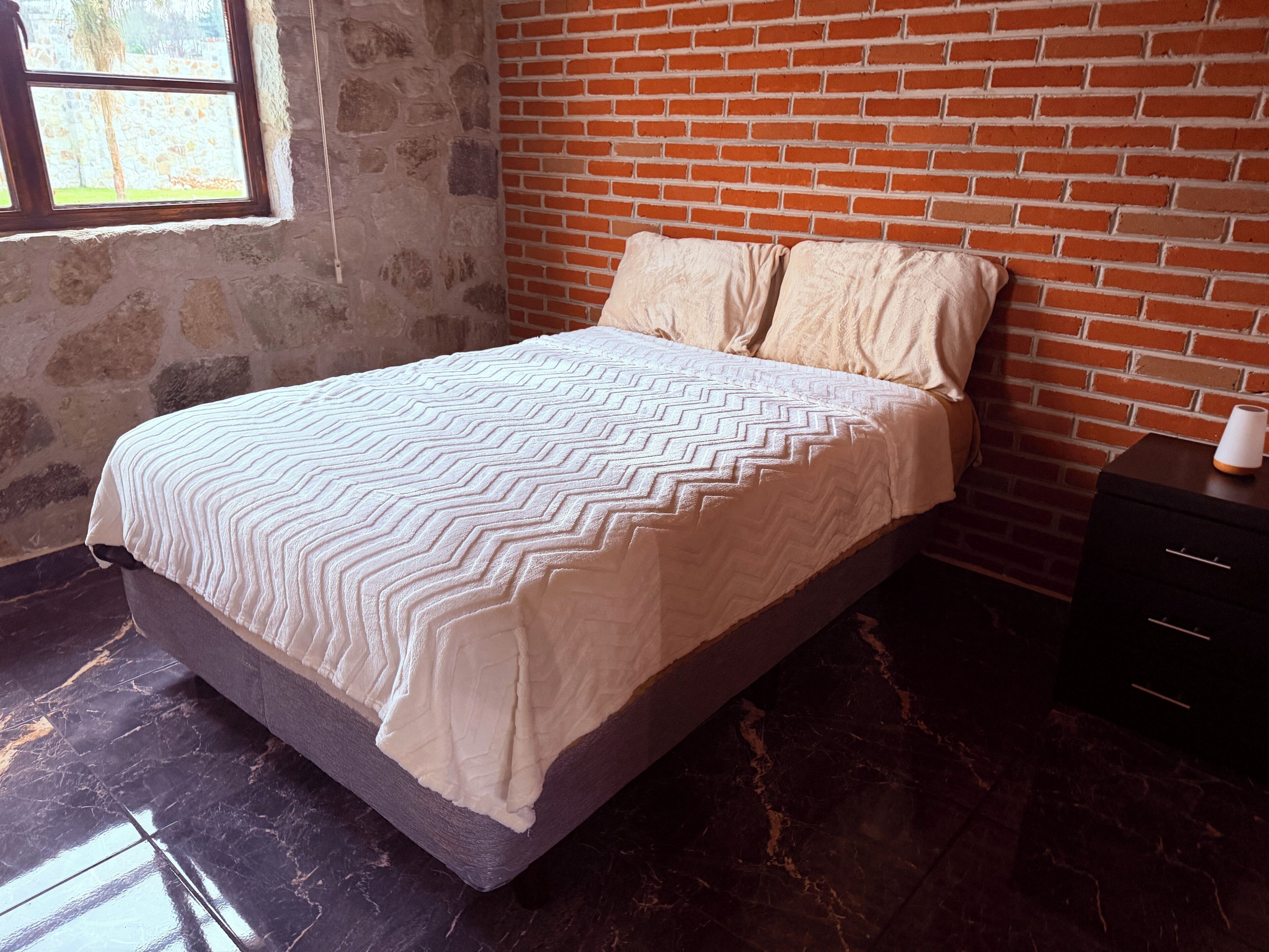 Un lit recouvert d’une couette blanche, dans une pièce dont les murs sont en briques et en pierre.
